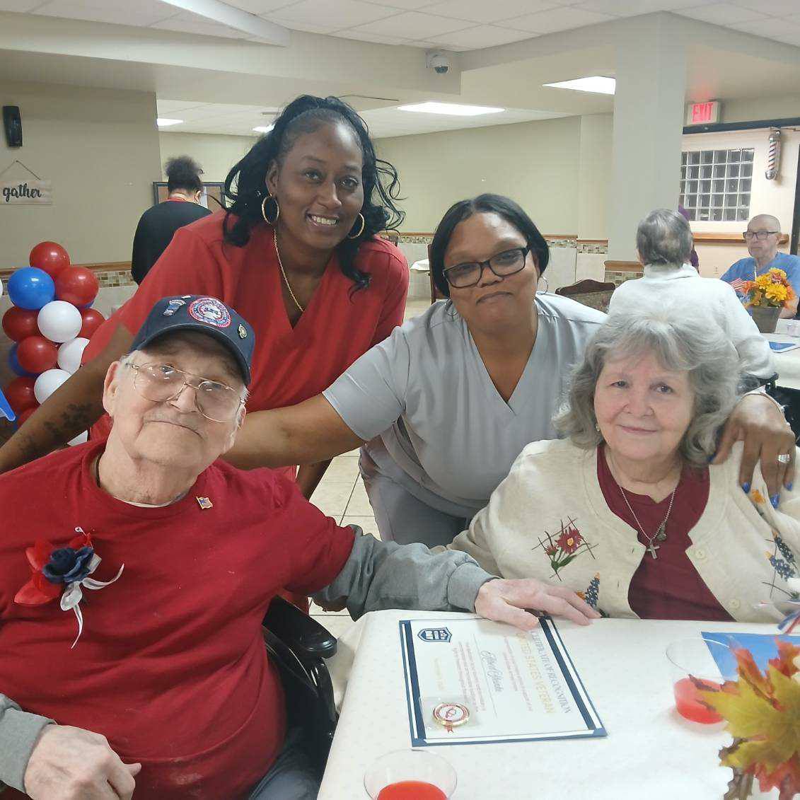 Residents and caregivers at Cedar Woods Assisted Living in Belleville, Michigan celebrating a veterans' appreciation event with American flags and certificates.