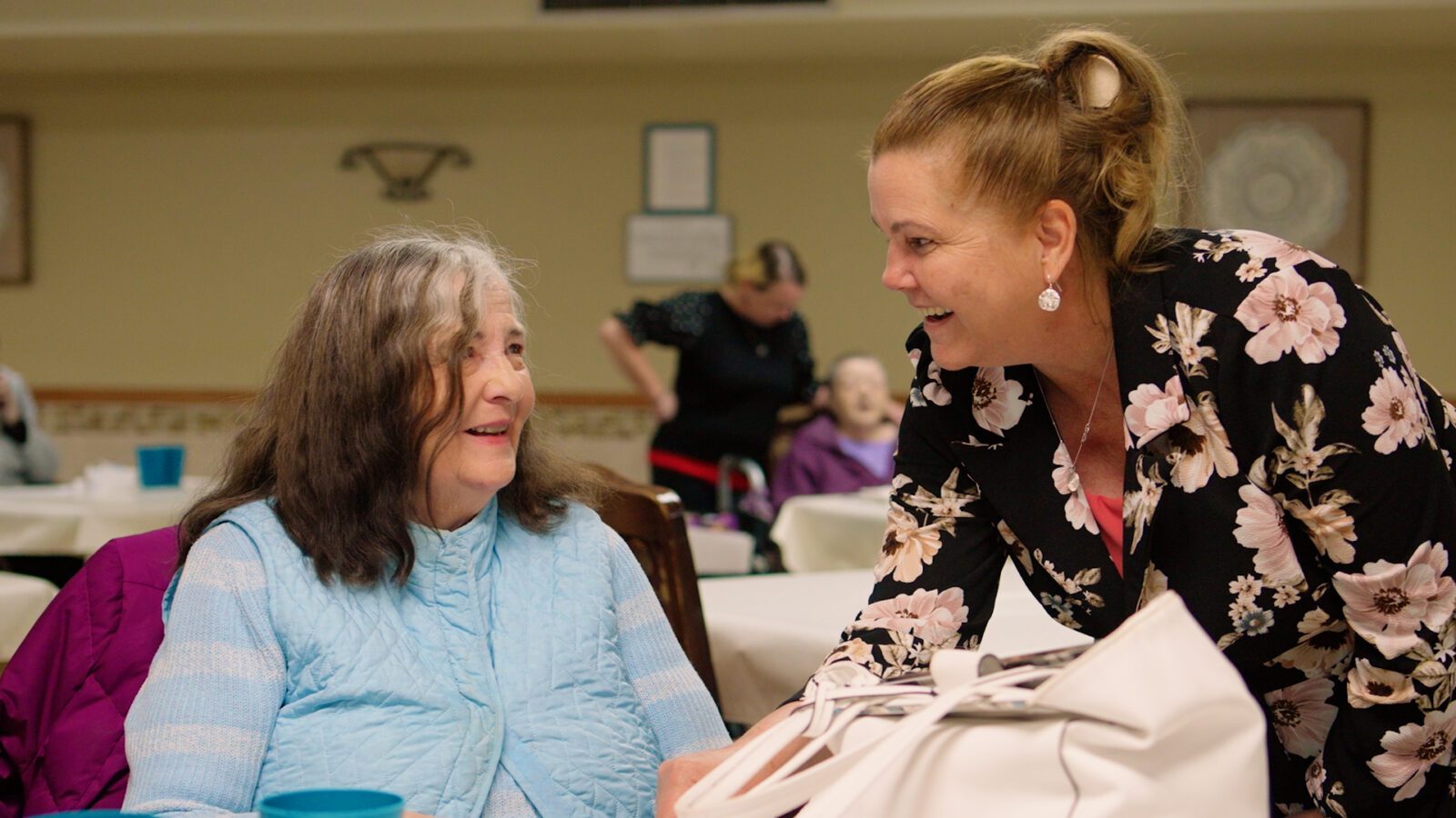 Cedar Woods Assisted Living near me team member warmly interacting with a smiling resident inside the Belleville, Michigan facility, highlighting compassionate senior care and community connection.